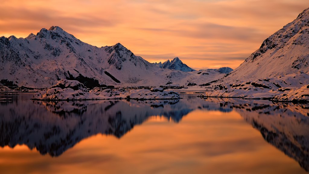 Orange sunset in fjord with snowy mountains in background, Lofoten