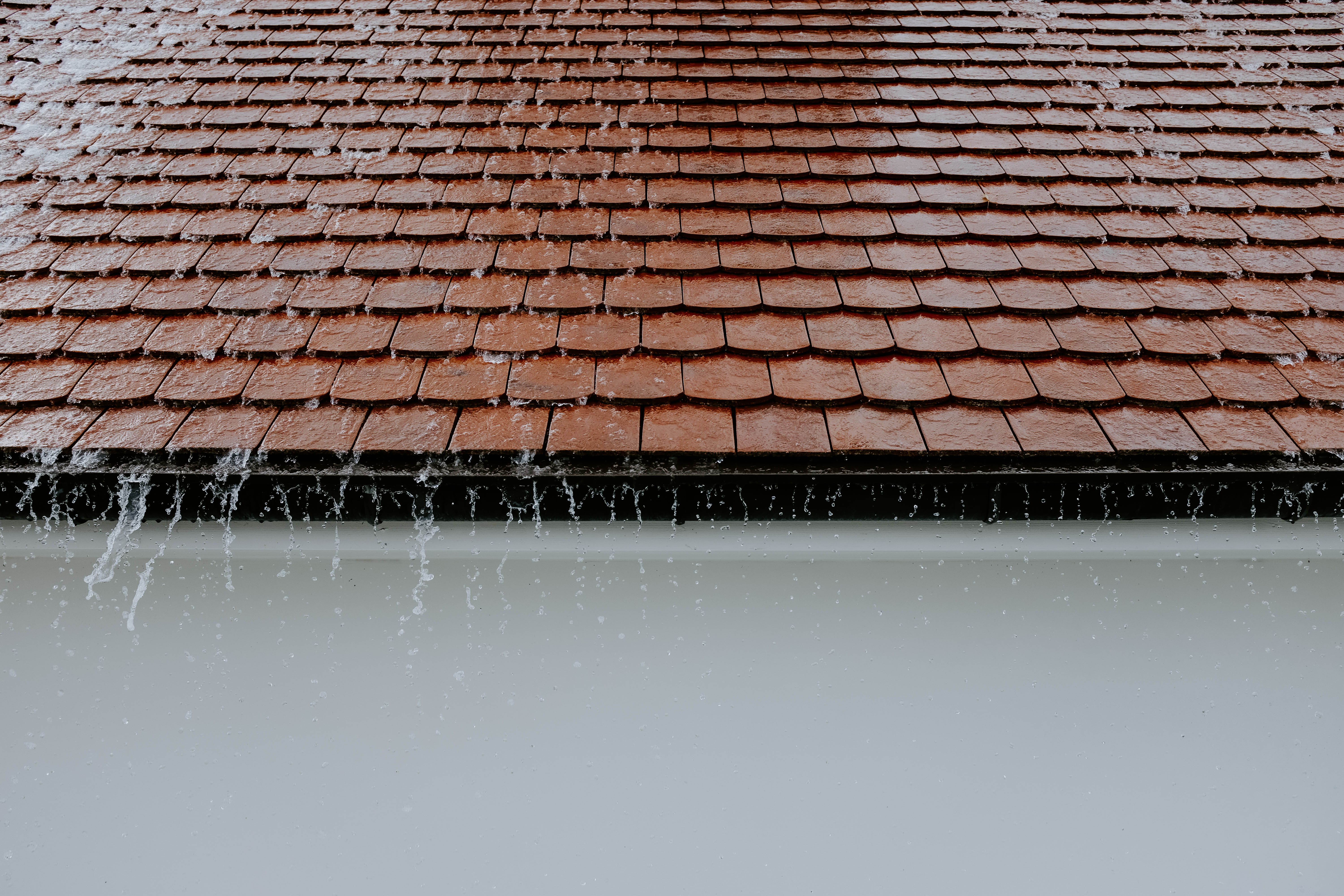 Rain cascading over roof tiles, highlighting the need to check roof surfaces and runoff before wet weather.