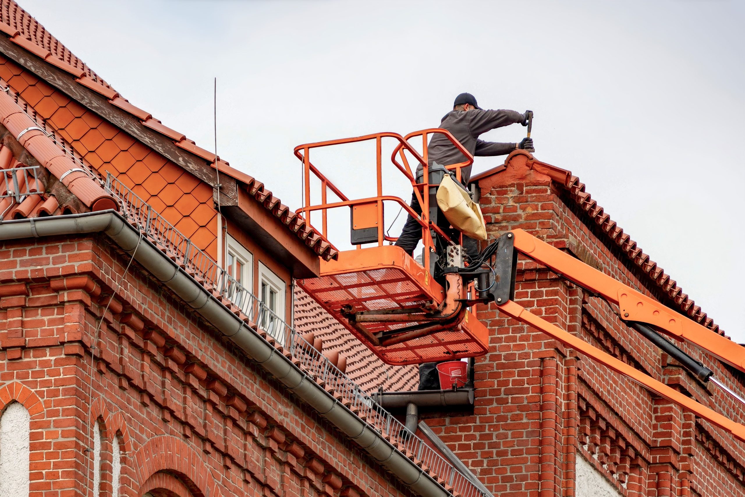 Roofer inspecting and maintaining the tiled roof of a large brick venue.
